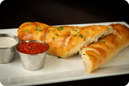 Stromboli on a white plate with a side of different sauces